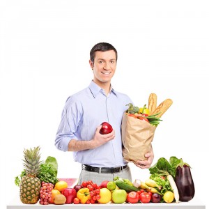 Smiling man holding an apple and bag with food products, posing