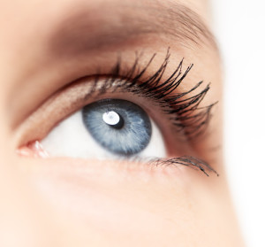 Closeup of human eye with blue pupil and long eyelashes over whi